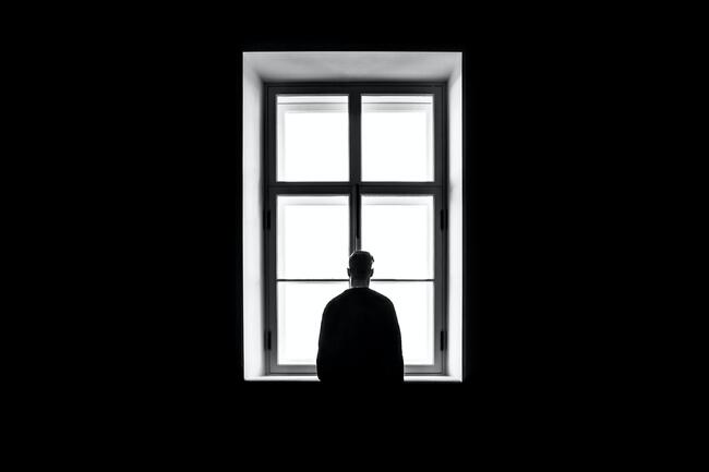 Sort hvitt fotografi av person som står foran et vindu