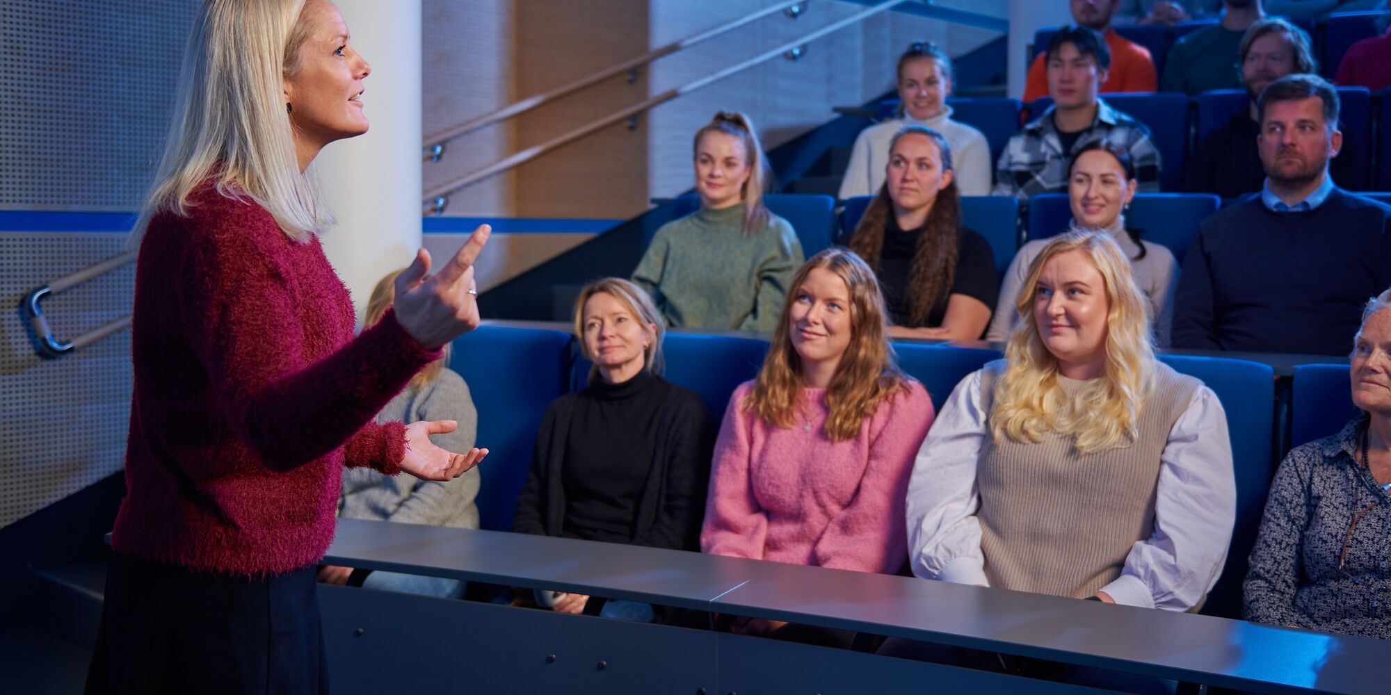 Foreleser står foran konferansedeltagere i auditorium og holder innlegg. Illustrasjonsbilde.