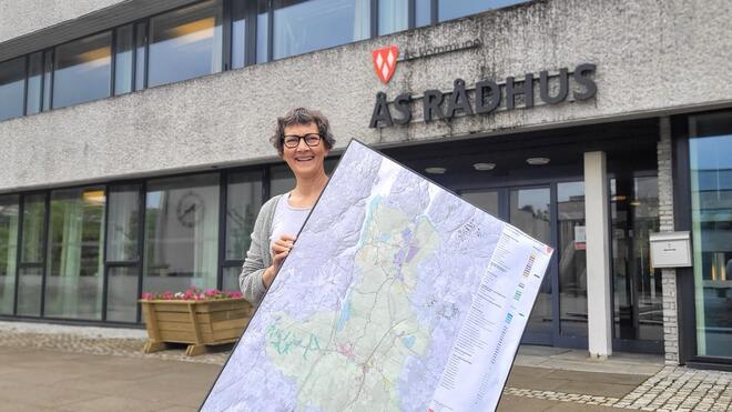 Solveig Viste i kommunens planavdeling står foran Ås rådhus med et plankart