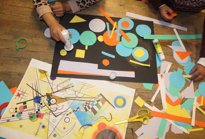 Barn limer ulike fargerike geometriske former på et sort A3 ark