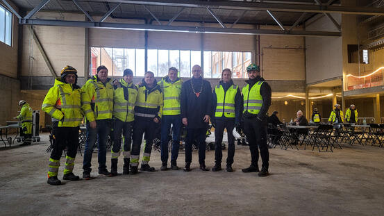 I midten står ordfører Ola Nordal og prosjektleder i Betonmast Lasse Kristiansen med noen utvalgte arbeidere i gule jakker rundt