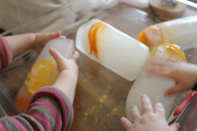 barnehender som tar på isklumper med appelsinskiver