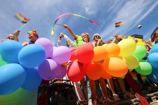 Glade folk som står bak regnbuefargede ballonger
