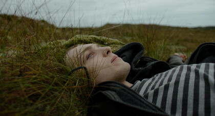 Stillbilde fra filmen, hovedpersonen ligger på bakken og ser opp i luften