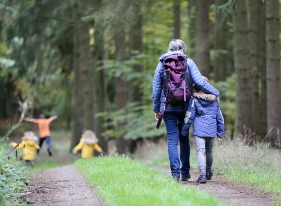 En dame og et barn går på en vei i en skog, foran dem løper mange flere barn