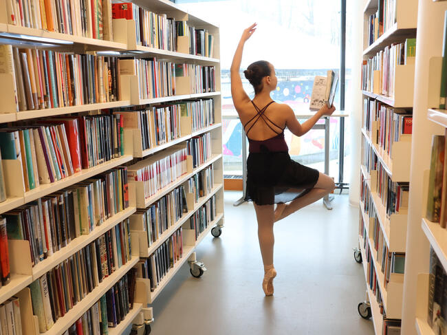 Ung dame danser ballett mellom bokhyllene i Ås bibliotek