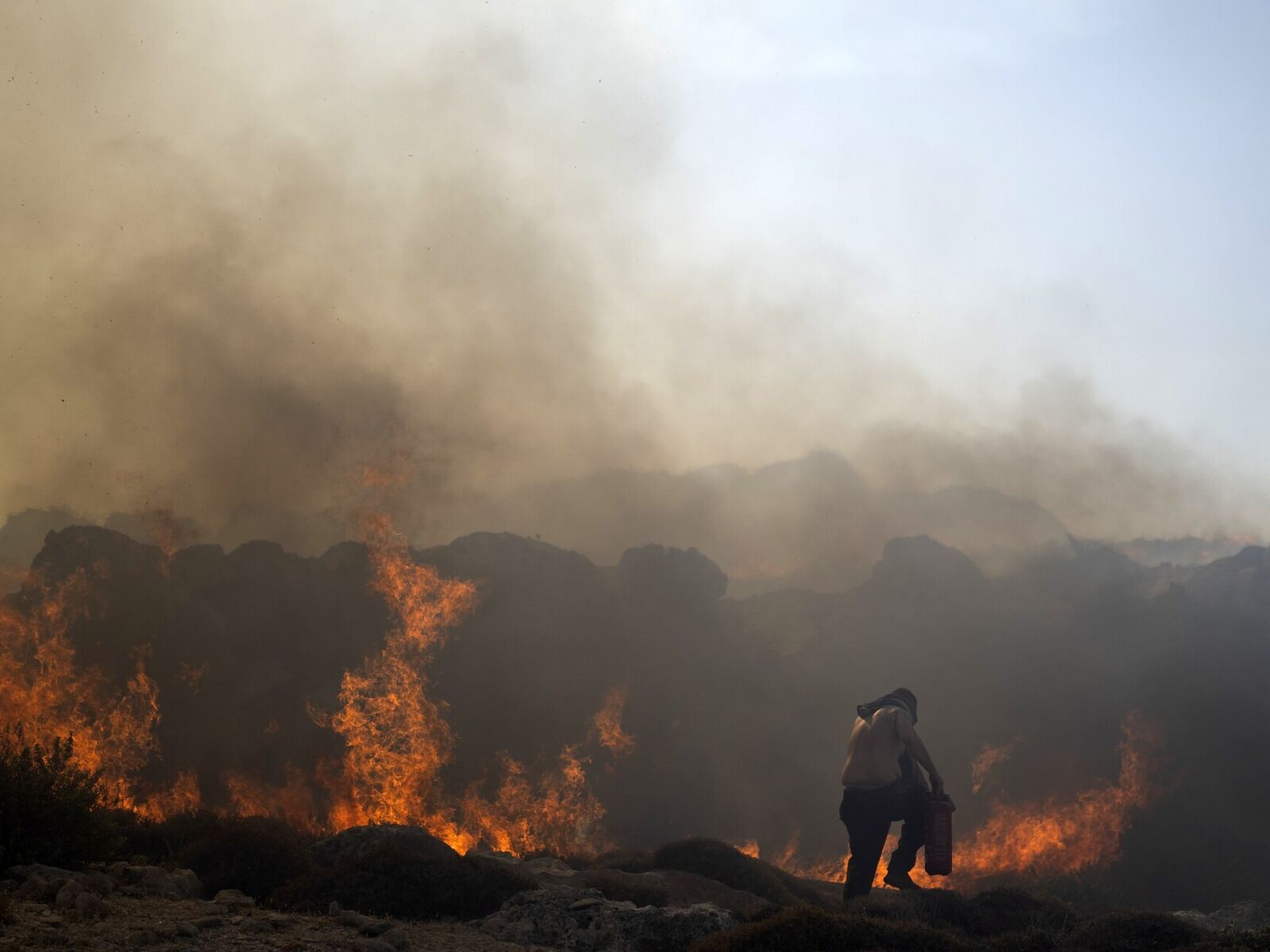 En mann forsøker å slukke en brann på Rhodos. Skogbrannene i Hellas herjer for niende dag på rad, og tallet på de som må evakuere fra hjemmene sine stiger stadig. Foto: Petros Giannakouris