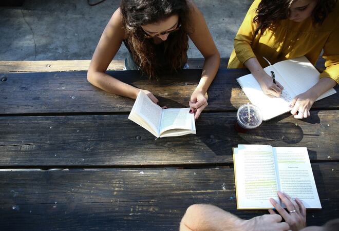 Tre unge personer sitter ute og leser og skriver