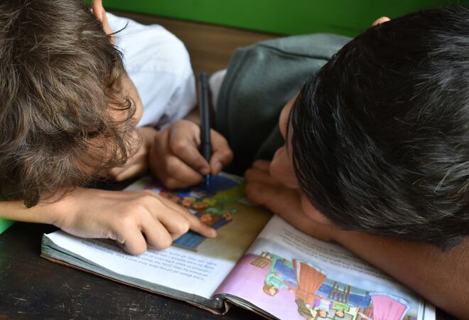 To gutter lener seg over en bok og skriver