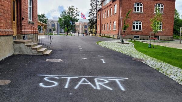 Asfalt med teksten START i hvitt, i bakgrunnen skolegården til Åsgård skole