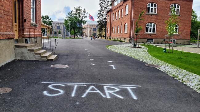 Asfalt med teksten START i hvitt, i bakgrunnen skolegården til Åsgård skole