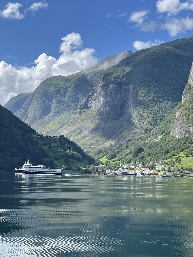 Båt som forlater underdal, fjord, fjell og hus