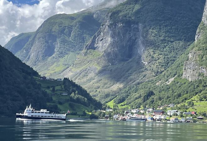 Båt som forlater underdal, fjord, fjell og hus