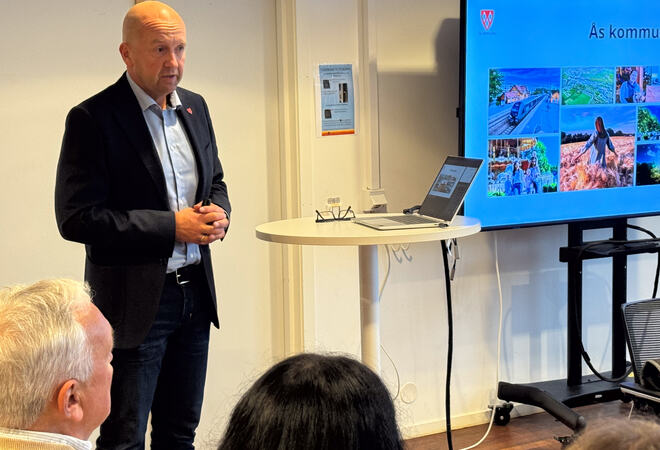 Kommunedirektør Tom-Arne Tørfoss la fram forslag til handlingsprogram med budsjett for formannskapet. Kommunedirektør Tom-Arne Tørfoss står foran en TV som viser bilder fra Ås
